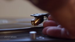 Eine Hand legt die Nadel eines Schallplattenspielers auf eine Schallplatte vorsichtig ab.