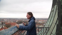 Ein Mann steht auf einem Balkon, von dem er über die Stadt schauen kann.