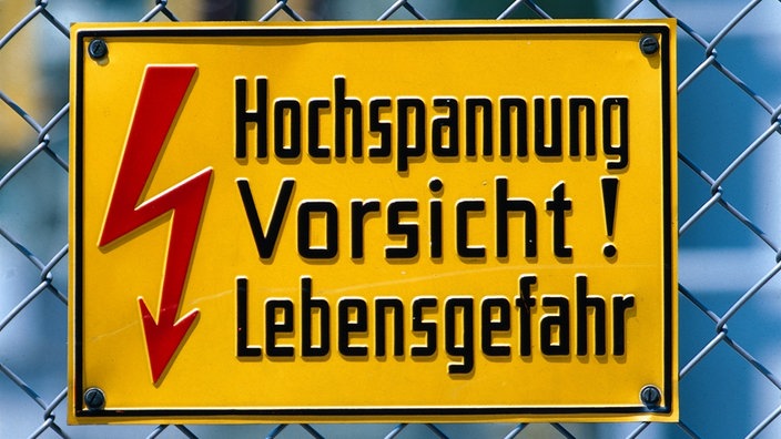 Ein Schild an einem Maschendrahtzaun weist auf die Gefahr durch Hochspannung hin | Bildquelle: Mauritius Ein Schild an einem Maschendrahtzaun weist auf die Gefahr durch Hochspannung hin