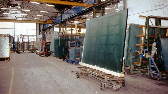In einer Industriehalle stehen verteilt mehrere große Glasplatten.