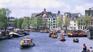 Das Bild zeigt einen Kanal in Amsterdam mit vielen Booten