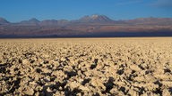 Blick über den ausgedörrten Boden der Atacama-Wüste auf Berge im Hintergrund.