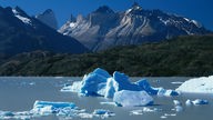Eisschollen treiben auf dem Lago Grey in Patagonien. Im Hintergrund steile Berggipfel.