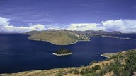 Steile Ufer am Titicacasee. Im See liegt eine kleine bewaldete Insel.