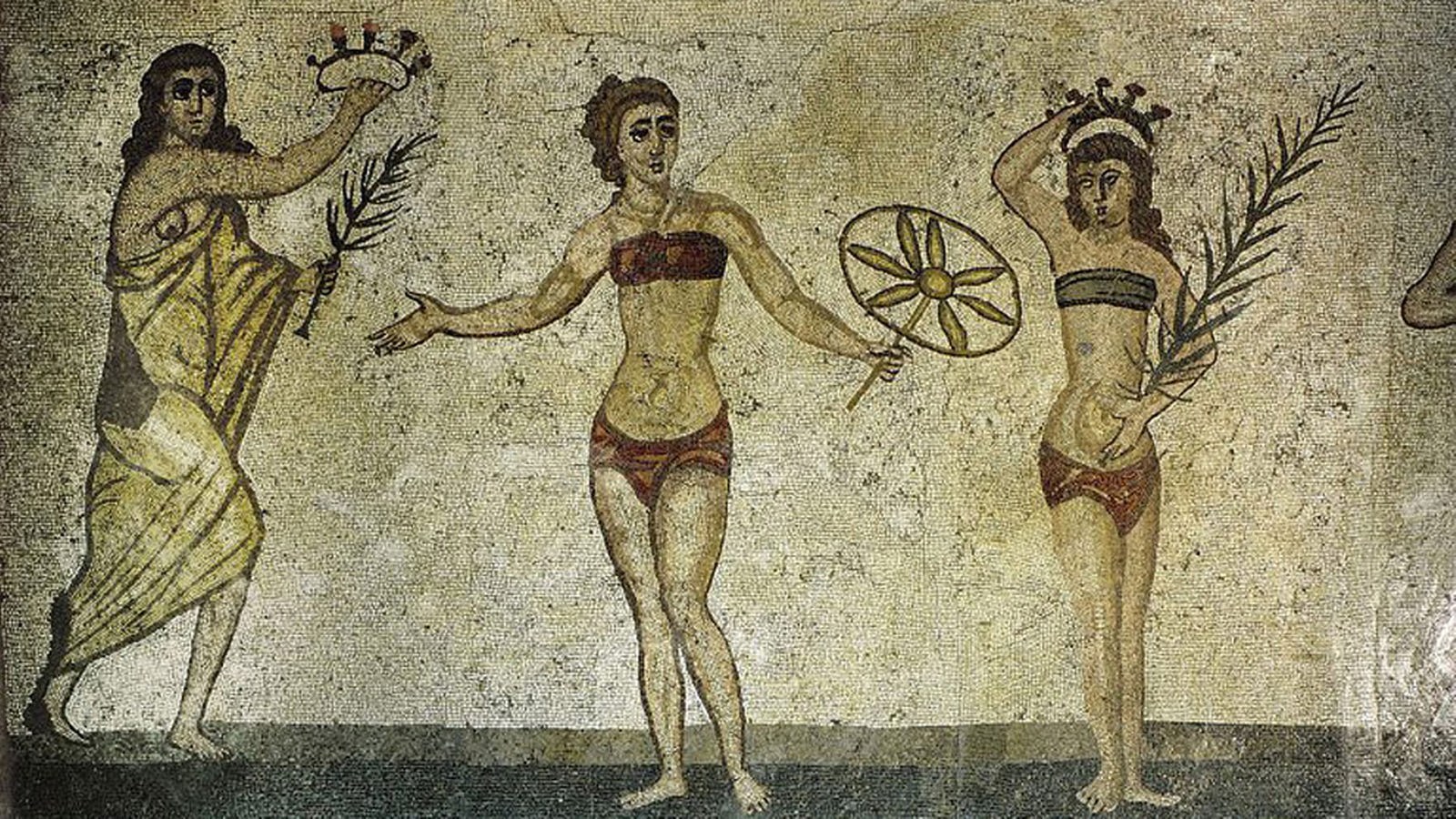 Altes Mosaik: Darauf sind zwei Frauen in einer Art Bikini zu sehen, links davon eine dritte in ein Gewand gehüllt.