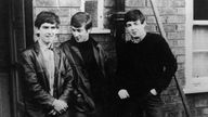 George Harrison, John Lennon und Paul McCartney stehen vor einer Wand (ca. 1960)