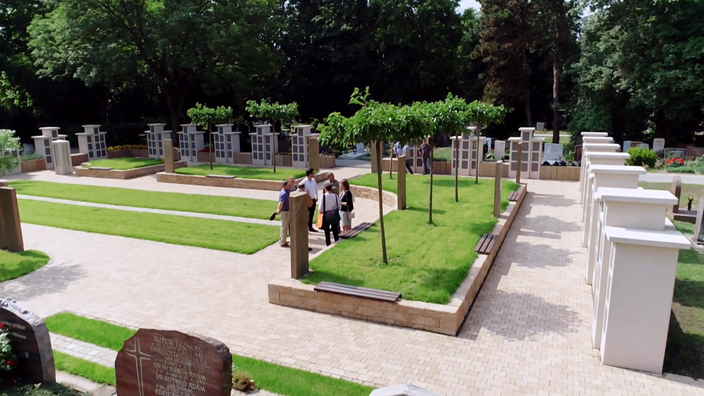 Eine Gruppe Menschen steht auf einem Friedhof. Um sie herum Gräber der Zukunft: Kolumbarien, Baum- und Erdrasenwahlgräber