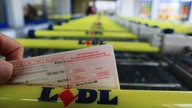 Eine Krankschreibungsformular wird hinter einen Einkaufwagengriff mit Lidl Schriftzug gehalten