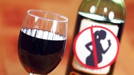Ein Glas Rotwein und eine Rotwein-Flasche mit dem Symbol "Nicht geeignet für Schwangere"