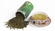 Loser grüner Tee in Dose und eine Tasse gekochter Tee