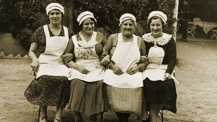 Schwarzweißfoto der 20er Jahre: Vier Dienstmädchen sitzen auf einer Bank