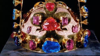 Vier große goldene Lilien, besetzt mit üppigen, farbenprächtigen Edelsteinen, wachsen aus einem goldenen Stirnreif hervor, der ebenfalls mit blauen, roten und pinkfarbenen Edelsteinen besetzt ist. Auf dem Scheitelpunkt steht ein goldenes Kreuz. | Bildquelle: akg Vier große goldene Lilien, besetzt mit üppigen, farbenprächtigen Edelsteinen, wachsen aus einem goldenen Stirnreif hervor, der ebenfalls mit blauen, roten und pinkfarbenen Edelsteinen besetzt ist. Auf dem Scheitelpunkt steht ein goldenes Kreuz.