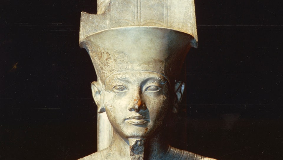 Skulptur des ägyptischen Gottes Amun aus dem Karnak-Tempel in Luxor. Der Gott ist mit einem langen Bart und einer hohen Kopfbedeckung nachgebildet. 