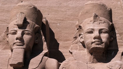 Zwei riesige Statuen der Pharaonen Ramses I. und Ramses II. Die Statuen sind aus rotem Stein gehauen und sind teilweise verwittert.