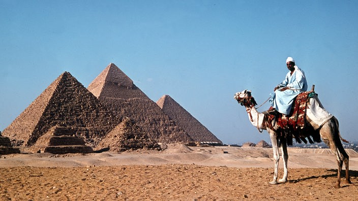 Blick auf die Pyramiden im Gizeh-Tal mit einem Reiter auf einem Kamel davor
