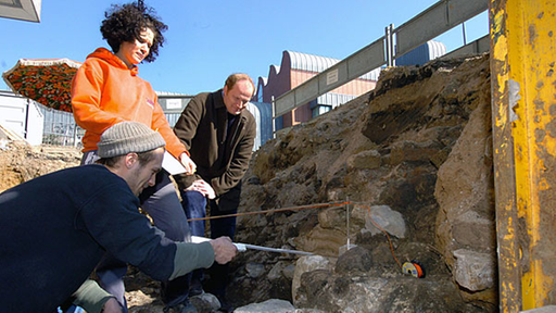 Zwei Archäologen vermessen und skizzieren den freigelegten Teil eines Mauerteils aus römischer Zeit.