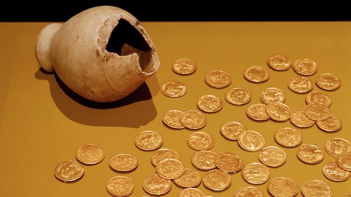 Eine zerbrochene Vase, daneben viele antike Goldmünzen