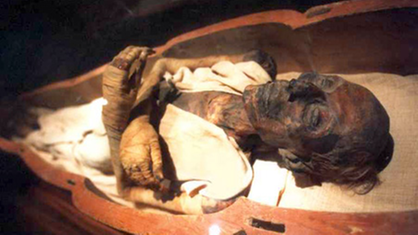 Großaufnahme von Kopf und Armen einer menschlichen Mumie in ihrem Sarkophag.