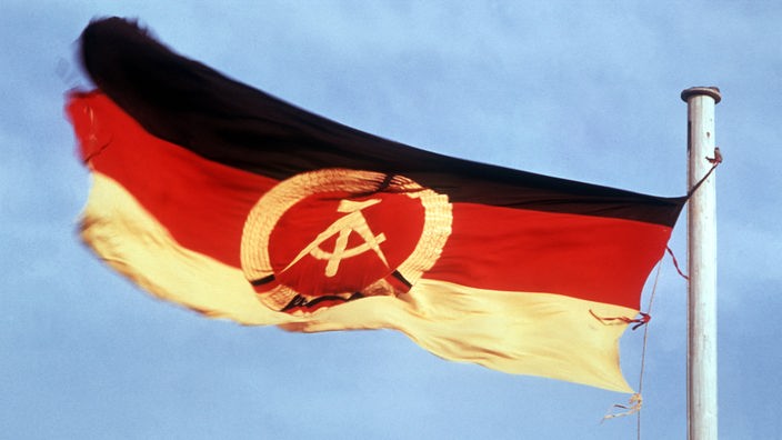 Die Flagge der Deutschen Demokratischen Republik: schwarz-rot-gold mit Hammer und Zirkel.