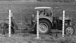 Schwarzweiß-Bild: Ein Traktor an einer Grenze mit Stacheldrahtzaun