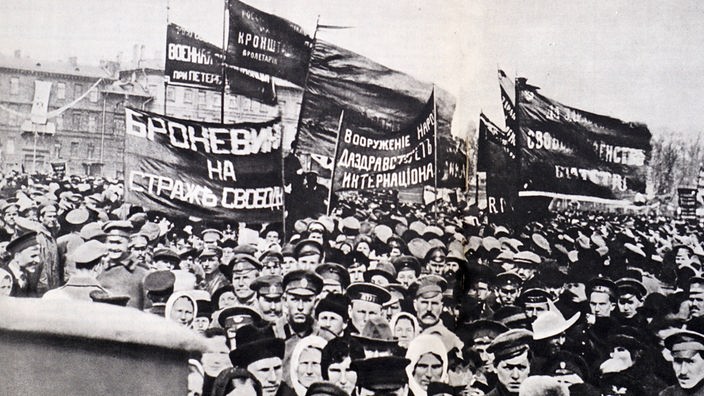 Schwarzweißaufnahme: Eine demonstrierende Menschenmenge mit Plakaten in russischer Schrift.
