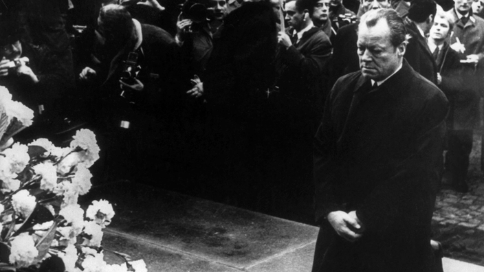 Willy Brandt kniet vor dem Denkmal im ehemaligen Warschauer Ghetto, vor ihm Kränze, hinter ihm eine Menschenmasse.