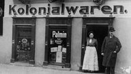 Zwei Menschen vor einem Kolonialwarenladen, ca. 1905