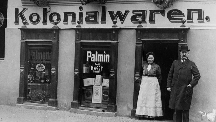 Zwei Menschen vor einem Kolonialwarenladen, ca. 1905 | Bildquelle: akg-images Zwei Menschen vor einem Kolonialwarenladen, ca. 1905