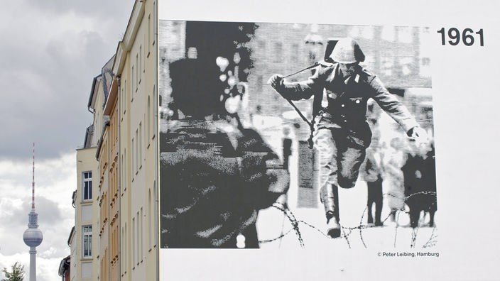 Ein DDR-Grenzpolizist springt zur Zeit des Mauerbaus 1961 über einen Stacheldraht in den Westen.