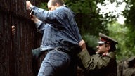 Ein Polizist versucht, einen Flüchtling am Übersteigen des Zaunes der Villa Lobkowicz zu hindern