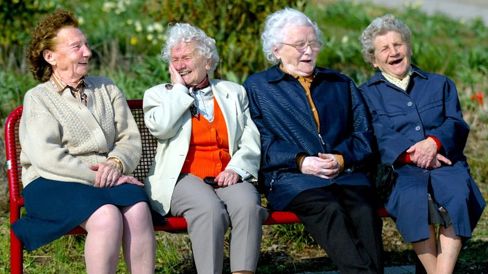 Vier alte Damen sitzen auf einer Parkbank und lachen