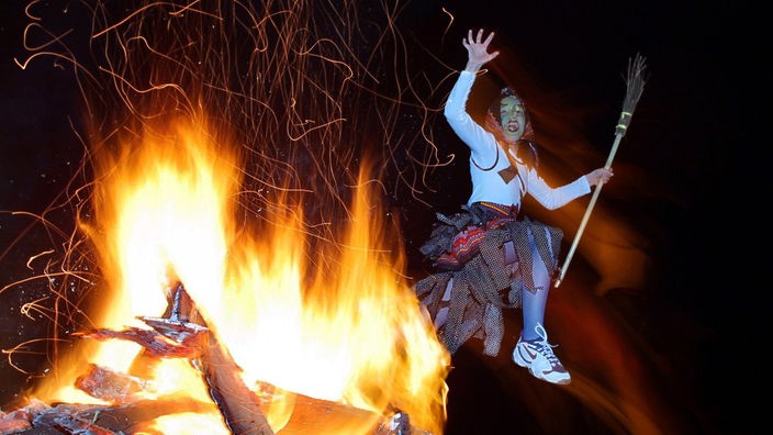 Als Hexe verkleidete Frau tanzt in der Walpurgisnacht um ein Feuer. 