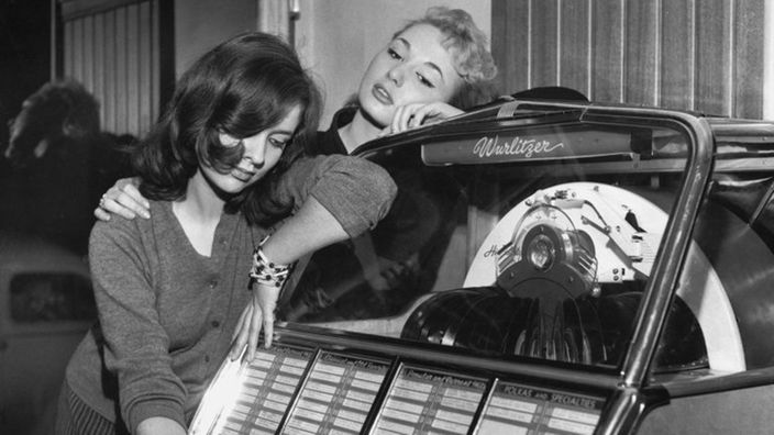 Auf dem Schwarzweiß-Bild sieht man zwei Mädchen an einer Jukebox stehen.