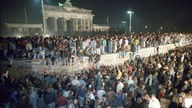 Eine Menschenmenge steht vor und auf der Berliner Mauer vor dem Brandenburger Tor