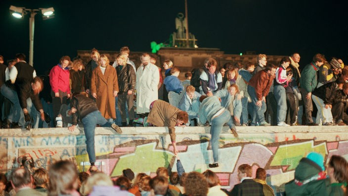 Menschen stehen auf der Berliner Mauer und ziehen andere mit nach oben