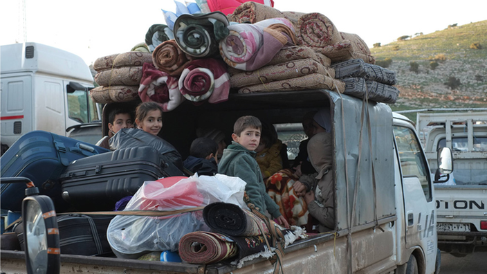 Kinder sitzen auf einem vollbepackten LKW an der türkisch-syrischen Grenze