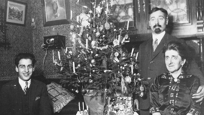Schwarz-weiß-Aufnahme von Georges Thomas mit seinen Eltern Maurice und Rosa Thomas neben einem Weihnachtsbaum.