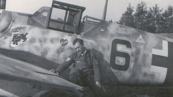 Schwarz-weiss Bild von Georg Fröhlich, wie er auf dem Flügel eines Fliegers sitzt.