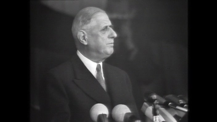 Schwarzweißaufnahme von Charles de Gaulle, der vor Mikrofonen steht.