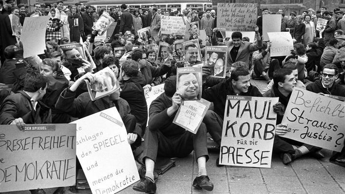 Schwarzweiß-Bild: Sitzende Demonstranten mit Plakaten.