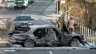 Ein völlig zerfetztes Auto steht quer auf der Straße. Kleine und große Autoteile liegen überall verstreut.