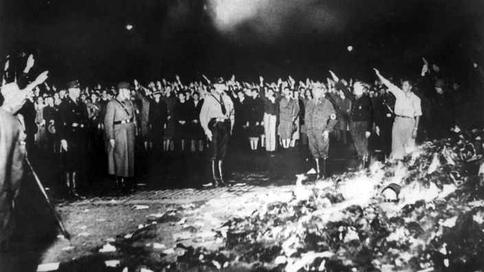 Schwarzweiß-Bild: Brennenden Haufen mit Büchern, im Hintergrund  SS-Leute und Schaulustige