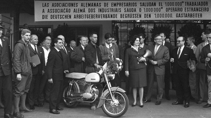 Schwarzweiß-Bild: Viele Menschen stehen um den millionsten Gastarbeiter und sein Moped herum | Bildquelle: dpa/Horst Ossinger Schwarzweiß-Bild: Viele Menschen stehen um den millionsten Gastarbeiter und sein Moped herum