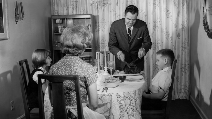 Schwarzweiß-Bild: Vater schneidet Braten an, die Familie sitzt am Esstisch | Bildquelle: WDR/Interfoto/LP Schwarzweiß-Bild: Vater schneidet Braten an, die Familie sitzt am Esstisch