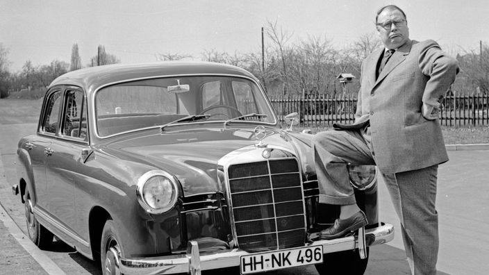 Heinz Erhardt mit Fuß auf der Stoßstange eines Mercedes