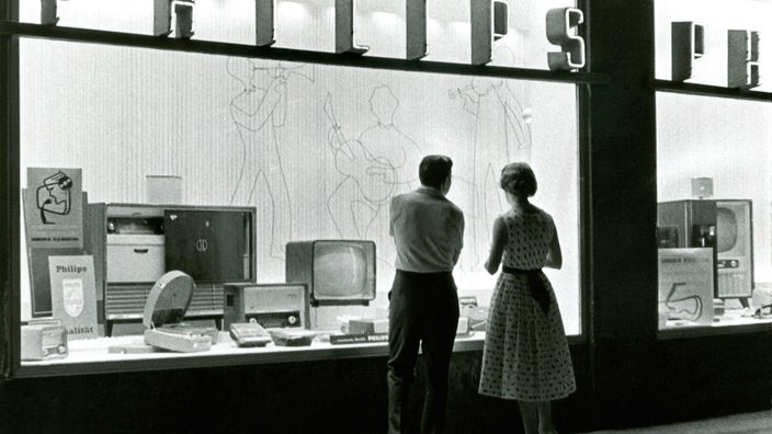 Schwarzweiß-Bild: Ein Paar steht vor dem Schaufenster eines Elektronik-Fachgeschäfts
