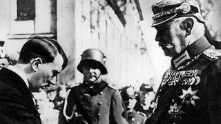 Hindenburg, in Wehrmachts-Uniform und hoch dekoriert mit Orden, schüttelt Hitler die Hand, der sich vor ihm verneigt.