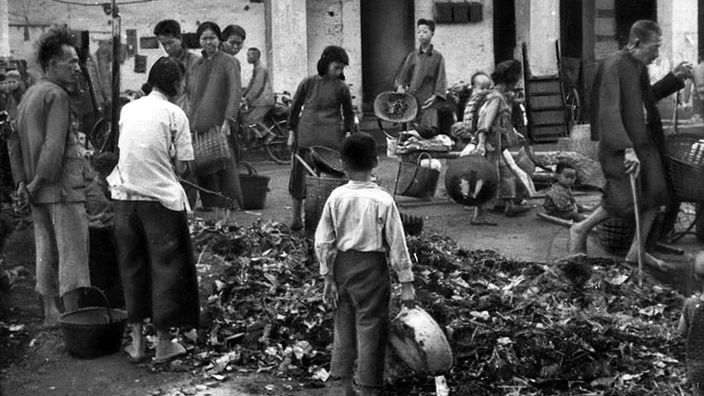 Schwarzweiß-Foto: Chinesen stehen um einen Haufen Altmetall herum