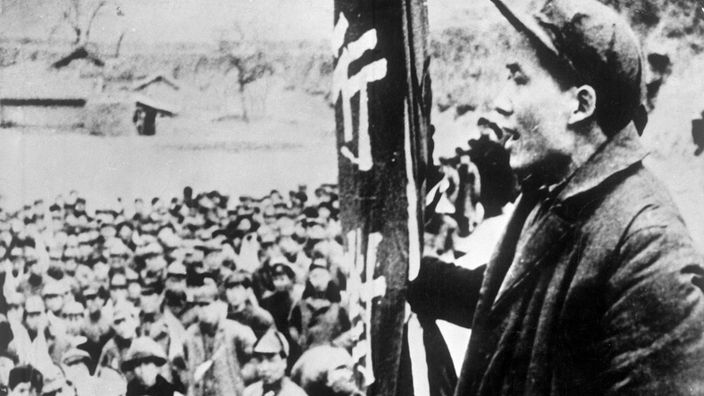 Schwarzweiß-Foto: Mit einer Fahne in der Hand spricht Mao zu einer Menschenmenge