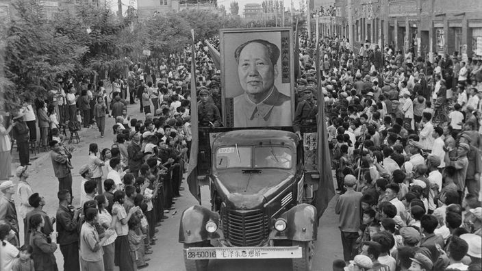 Ein Wagen mit einem riesigen Bild Maos fährt durch eine Straße, die von einer Menschenmenge umsäumt wird